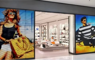 Retail storefront window fitted with digital display screens showing fashion advertising